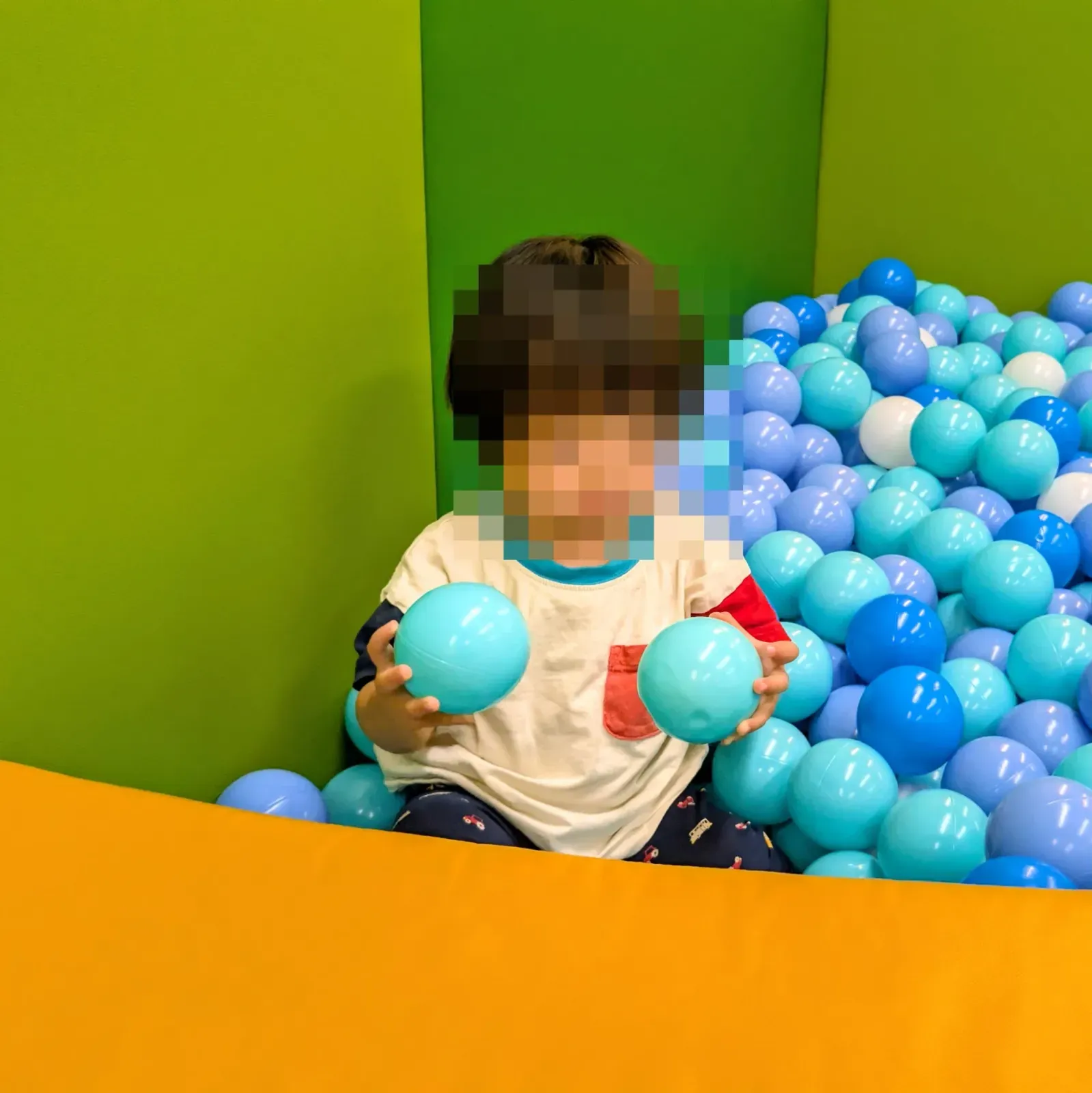 ピュアハートキッズランドのボールプールで青いボールを両手に持つ1歳7ヶ月の息子